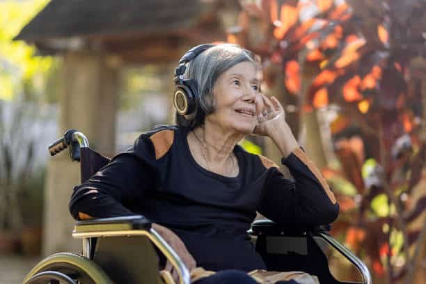 asian senior woman listening music with headphone in backyard.