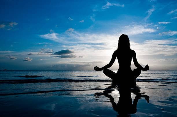 silhouette of woman in lotus position sitting in sea and medditating